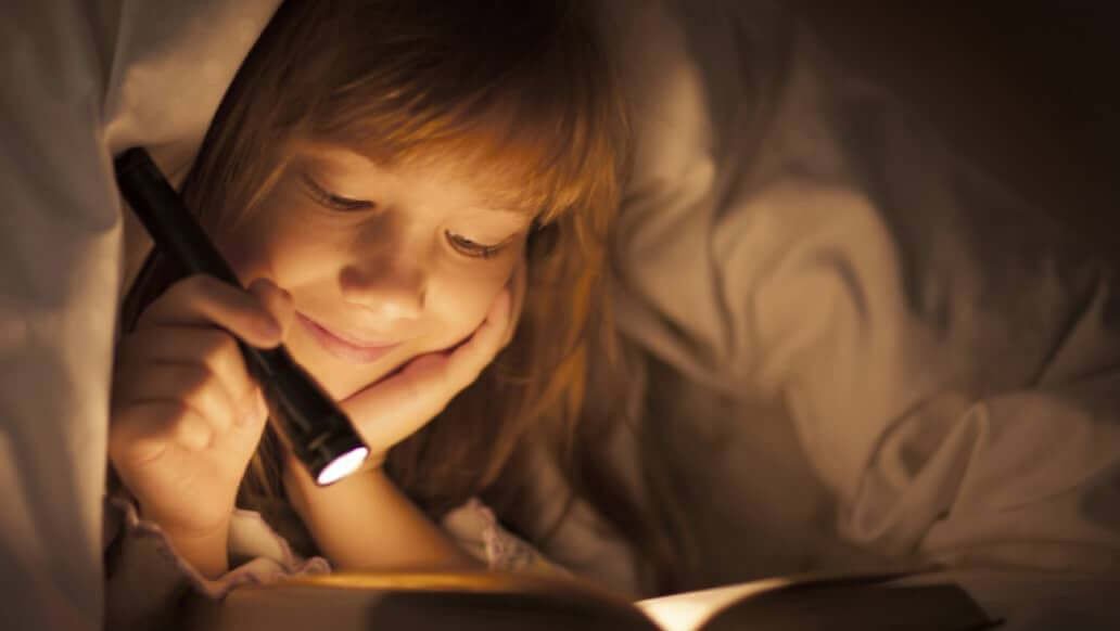 Child reading a book with a flashlight.